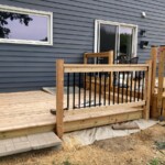 Added two posts, railings and balusters. The ground drops away quite a bit from the deck so we wanted the railing to prevent accidents. I used large pavers on top of a concrete base for a step to the ground. Deck railing installed, Paver step installed.